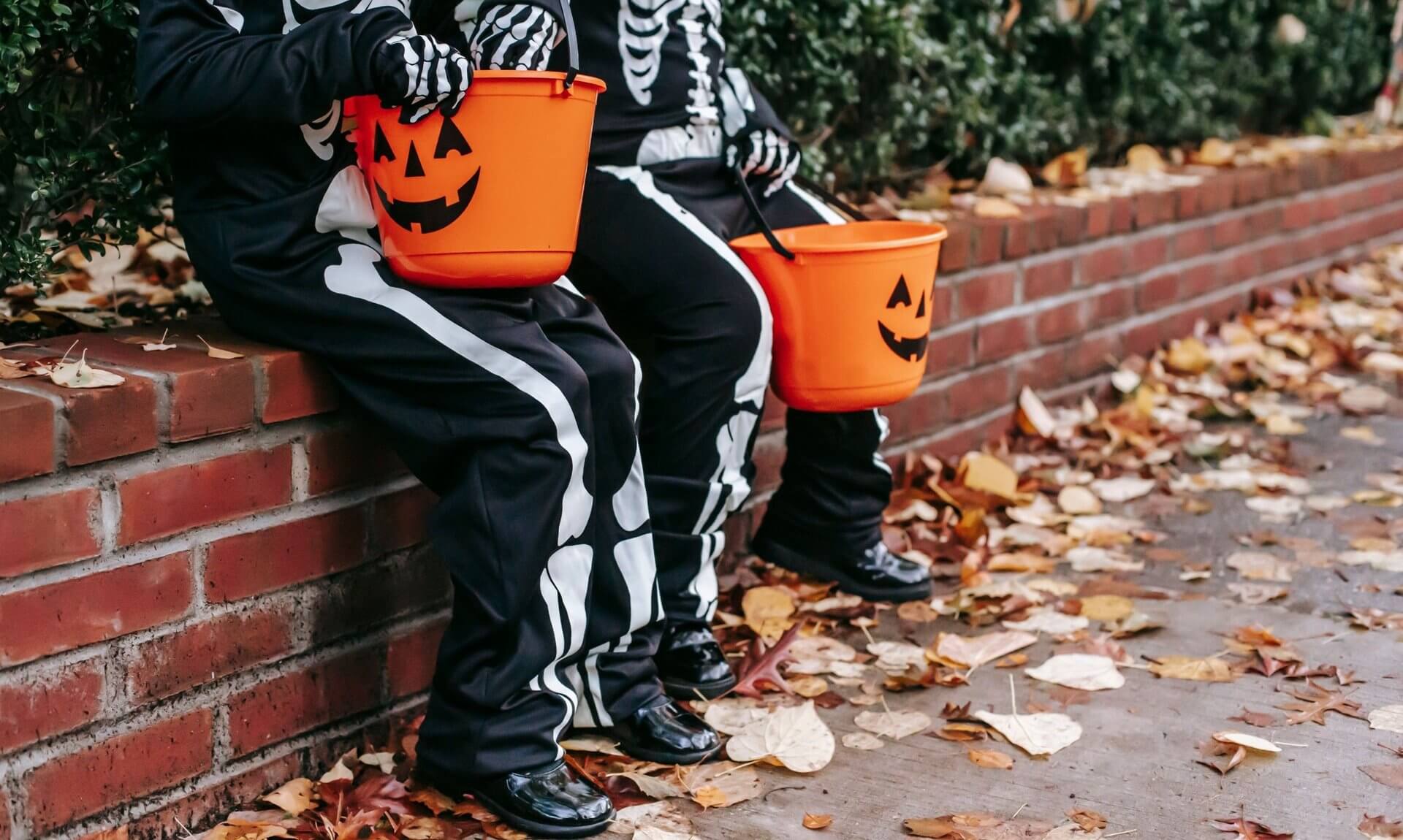 Two children in skeleton costumes holding pumpkin trick or treat buckets
