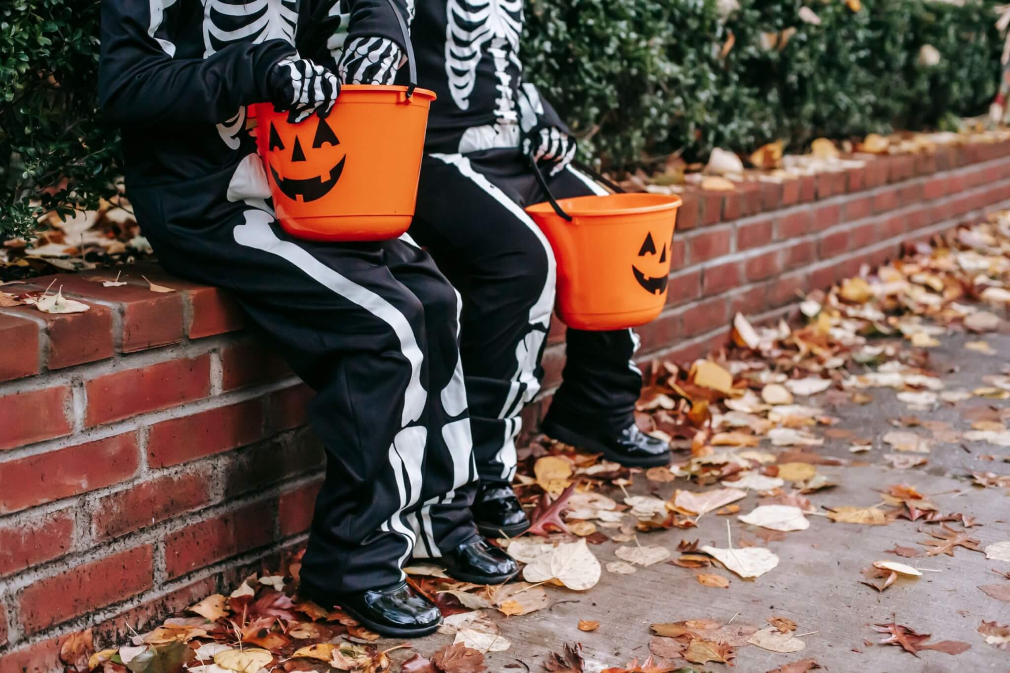 Two children in skeleton costumes holding pumpkin trick or treat buckets