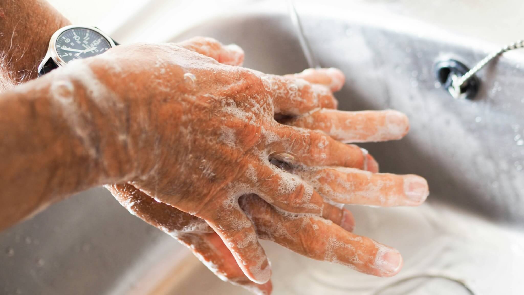 Close-up of hands lathered with soap over a sink