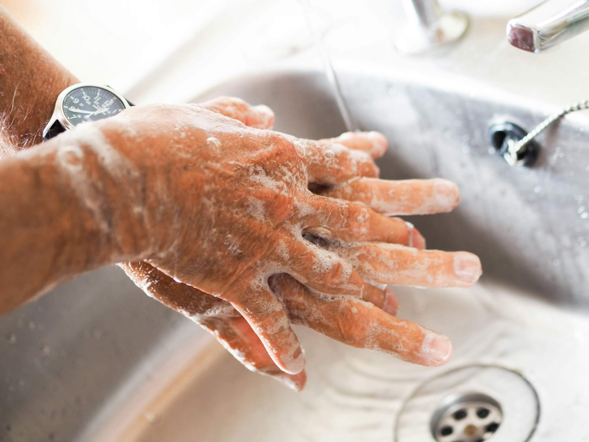 Soapy hands being washed under a running tap at a sink