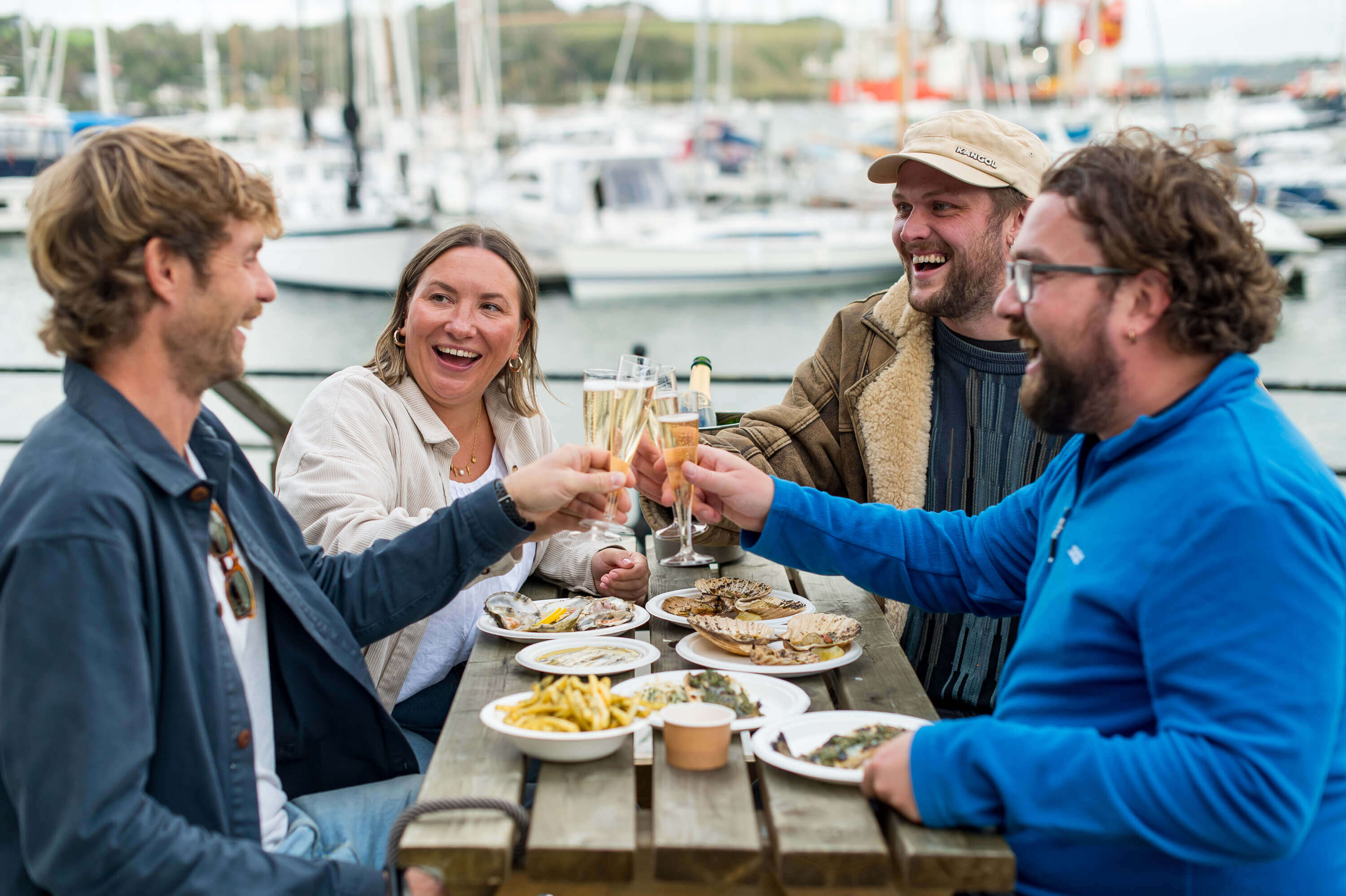 Friends raising a glass over plates of oysters by the harbour at Falmouth Oyster Festival