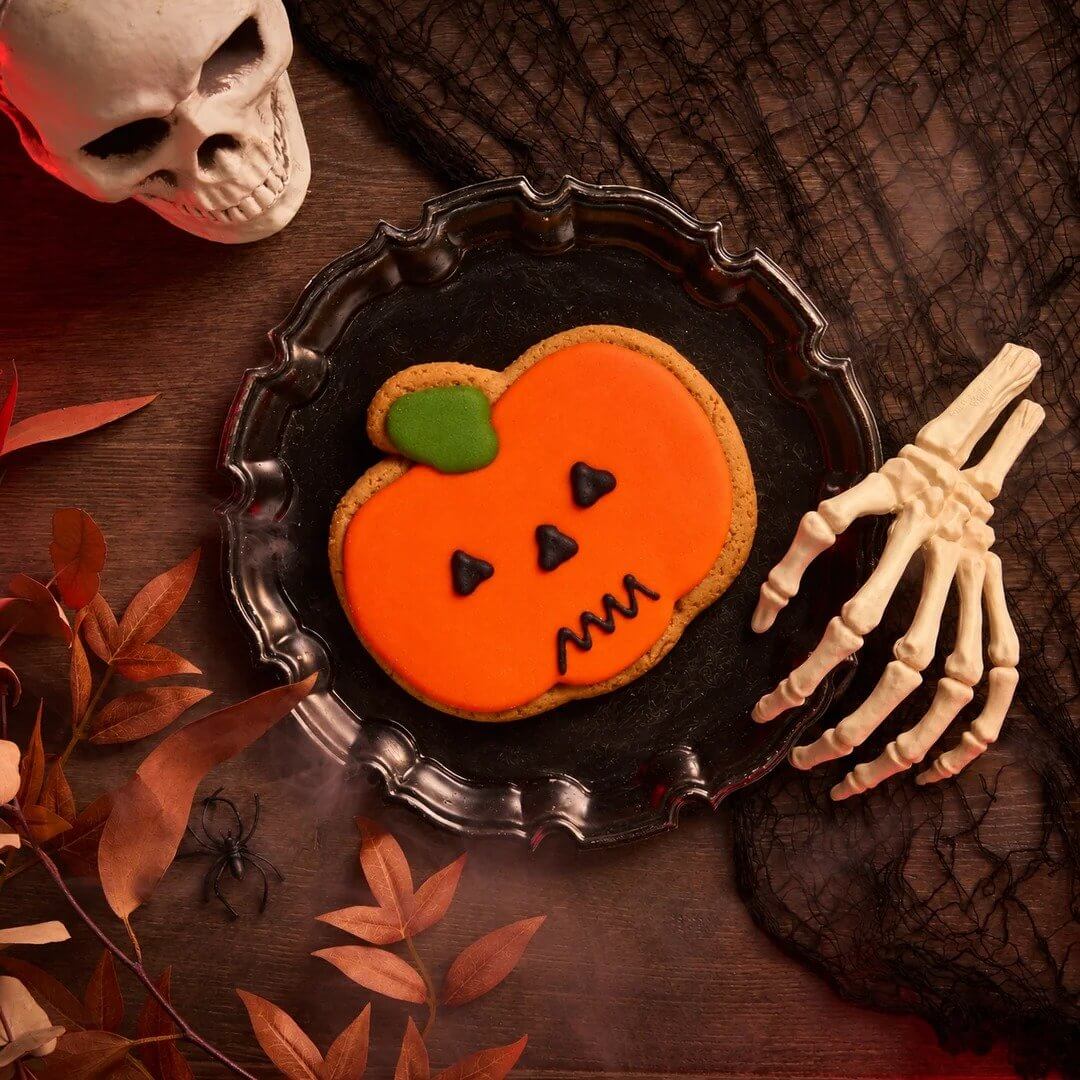 Iced pumpkin biscuit on a black plate with Halloween decorations