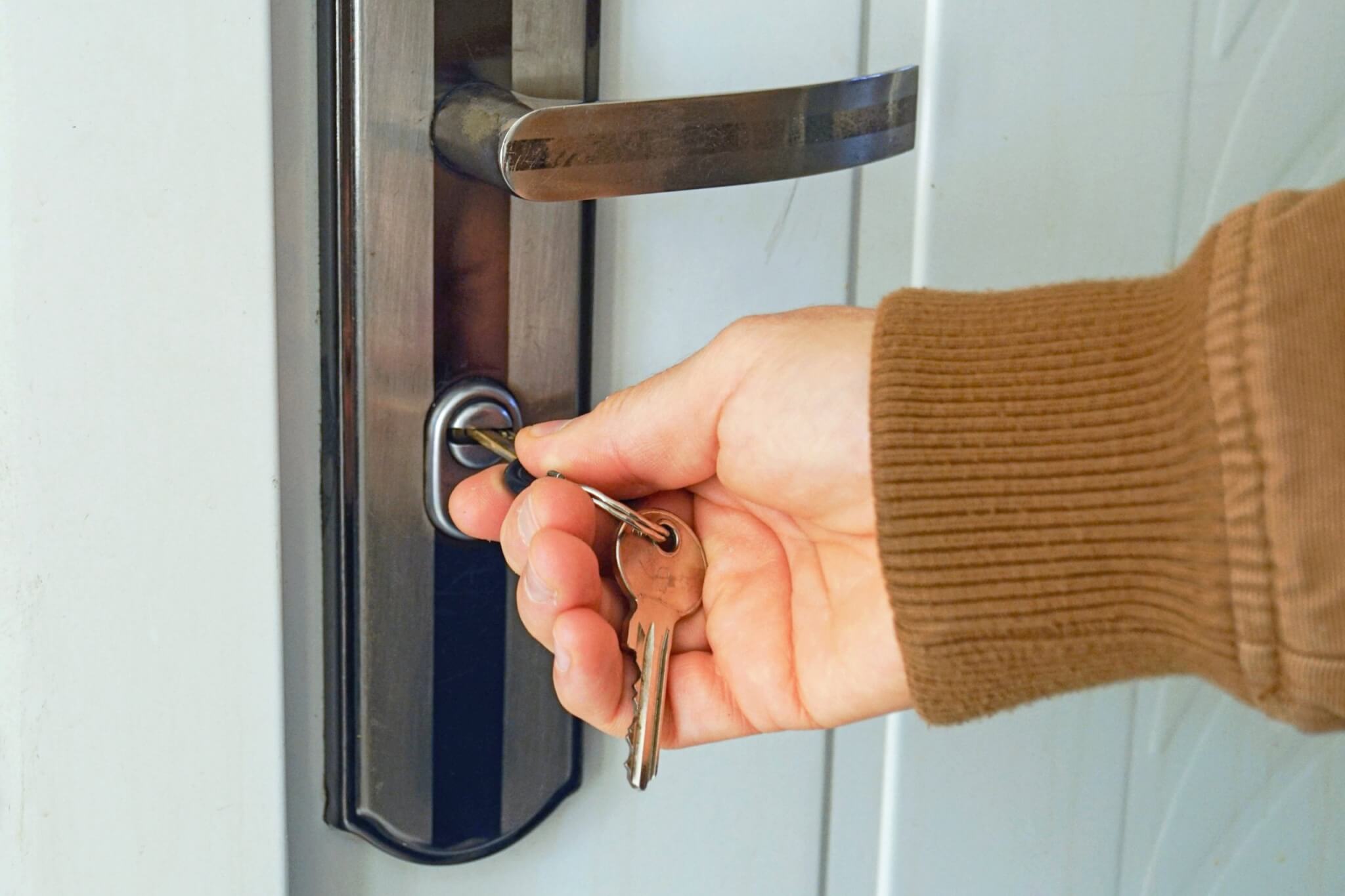 A hand in a brown jumper turning a key in a front door lock