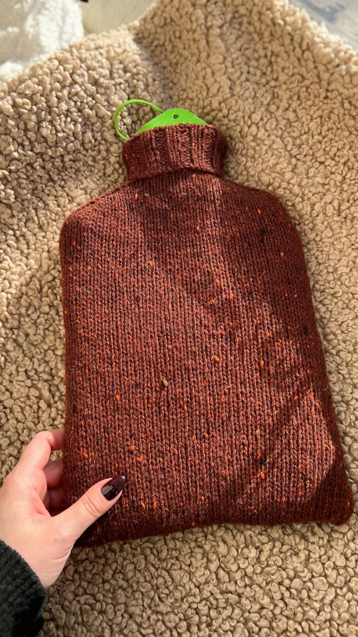 Hot water bottle in a knitted rust-coloured cover