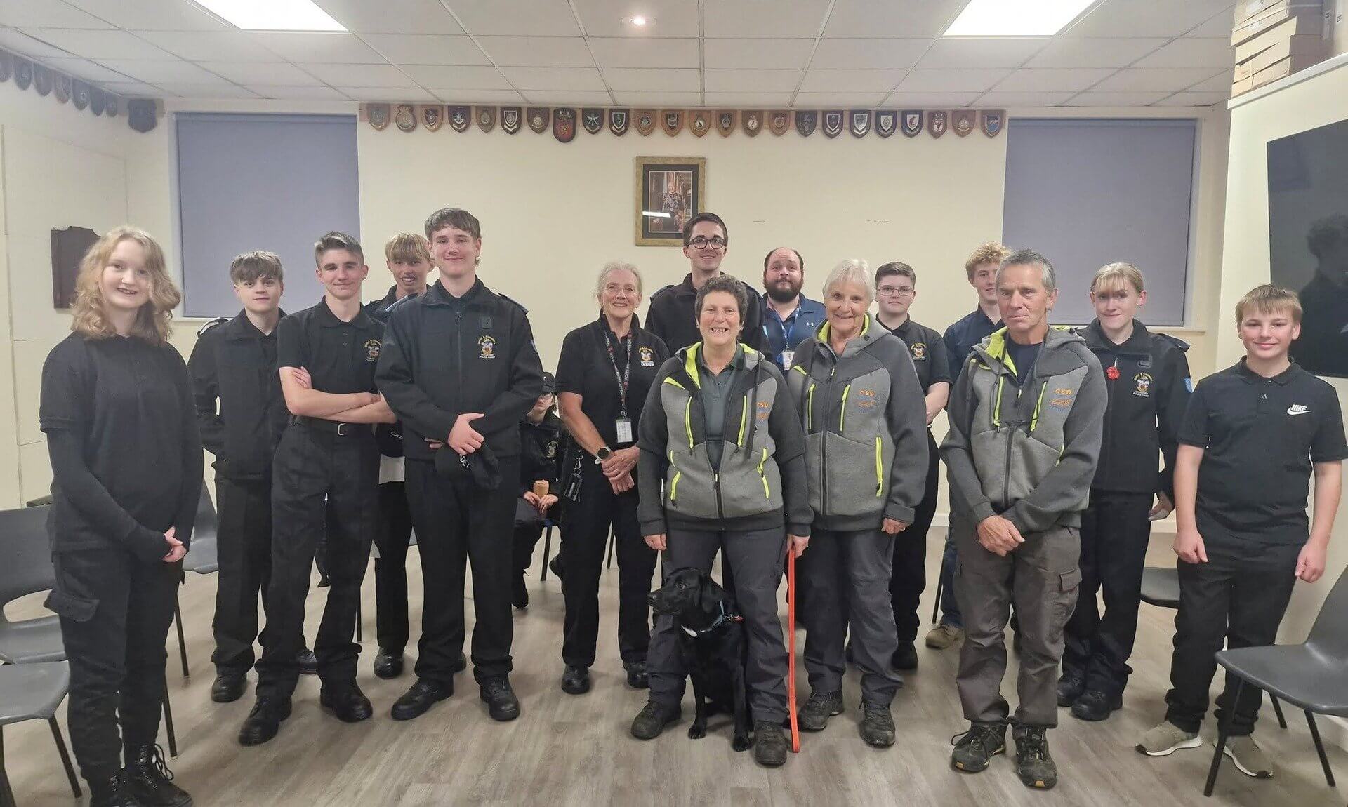 Launceston Police Cadets and Cornwall Search Dogs volunteers standing in a hall with a black search dog