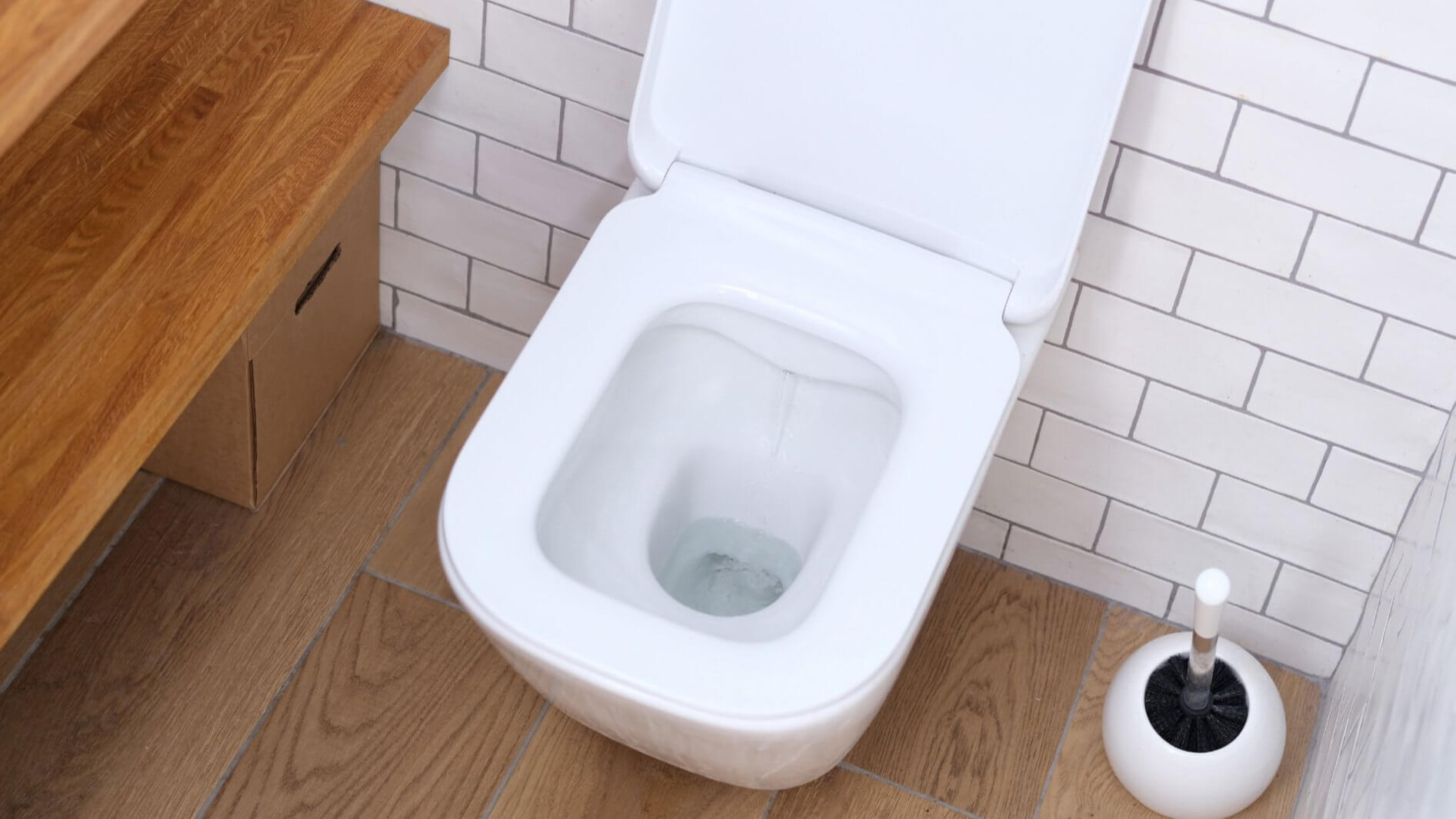 A white wall-hung toilet with the seat raised and water running into the pan