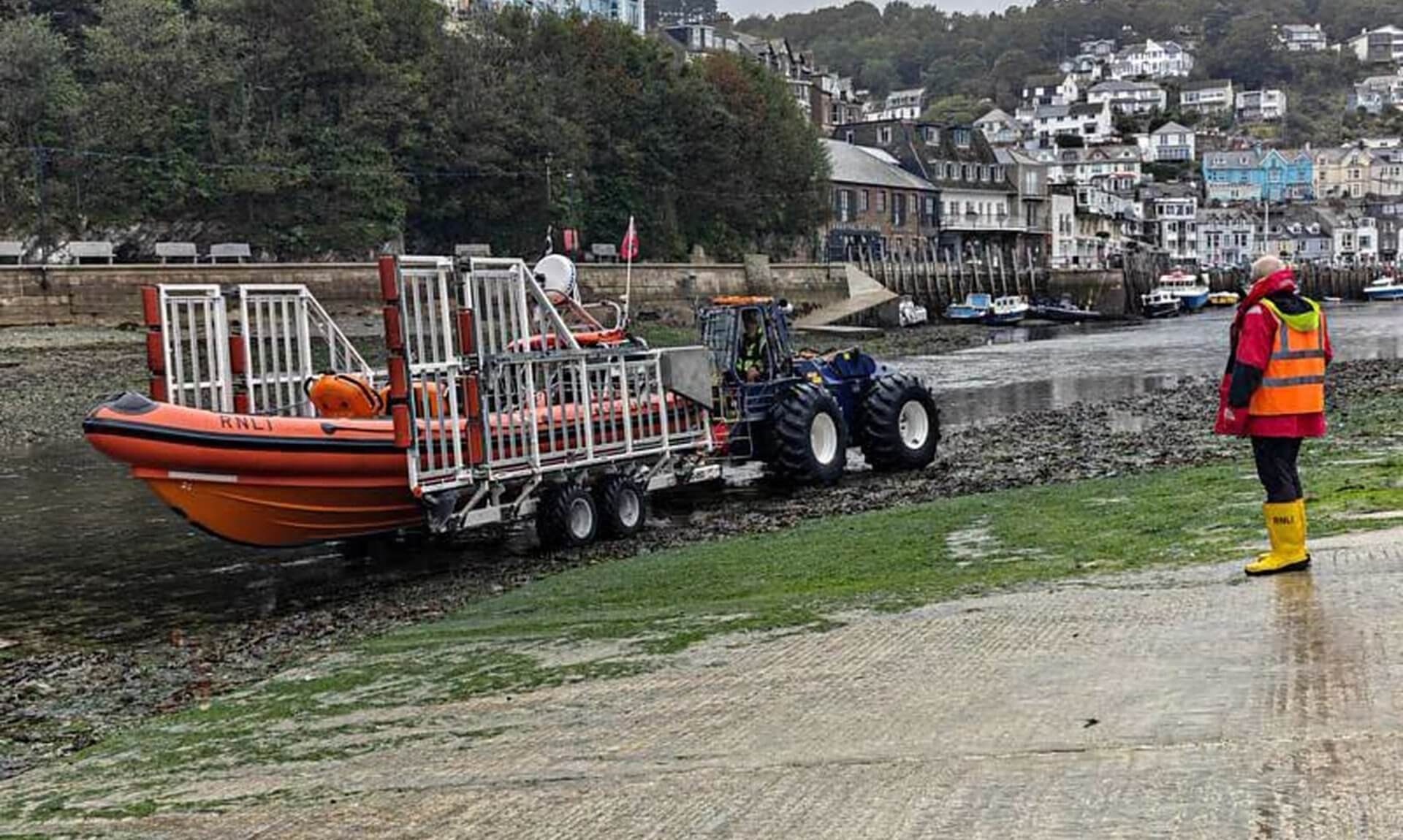 Looe RNLI inshore lifeboat on its launch trailer behind a tractor on the river bed at low tide