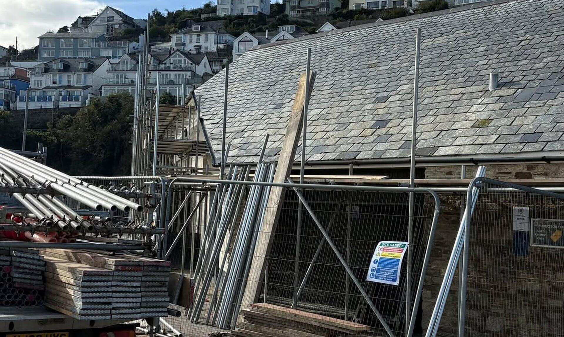 Scaffolding, fencing and a site safety sign around the slate-roofed seafront toilets in Looe