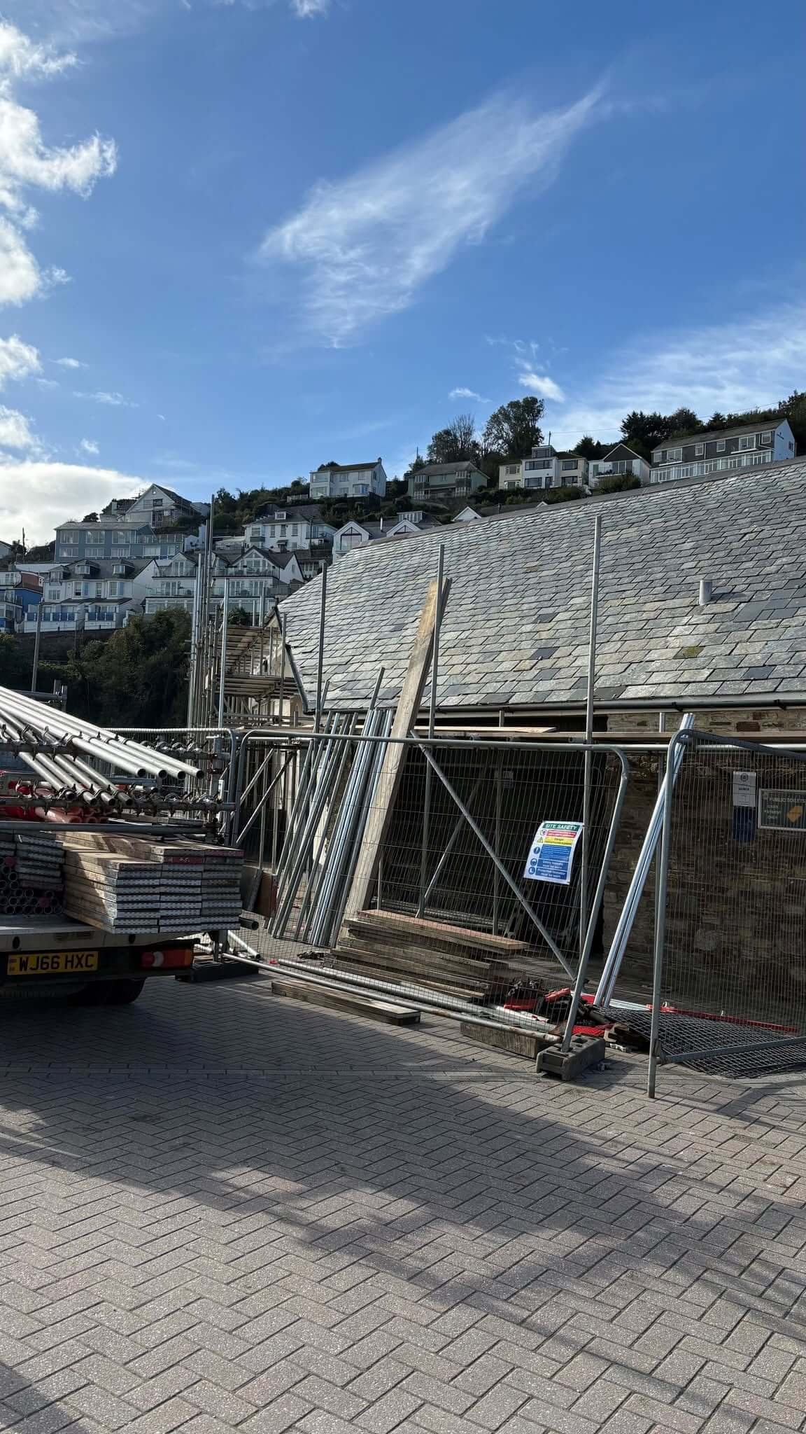 Scaffolding, fencing and a site safety sign around the slate-roofed seafront toilets in Looe