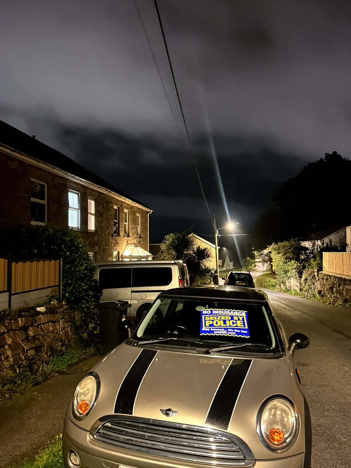 Mini seized by police with a police seizure notice in its windscreen on a West Cornwall street at night