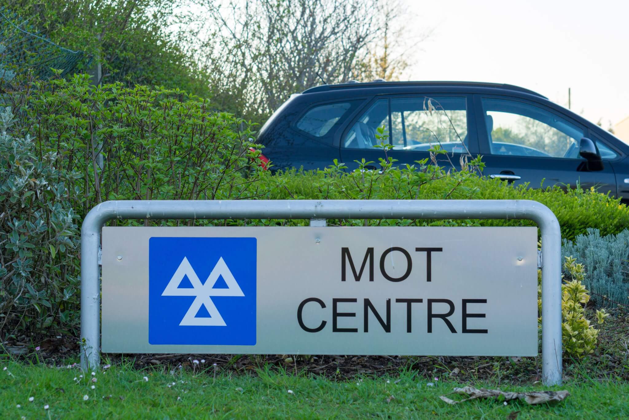 MOT centre sign with a car parked behind a hedge