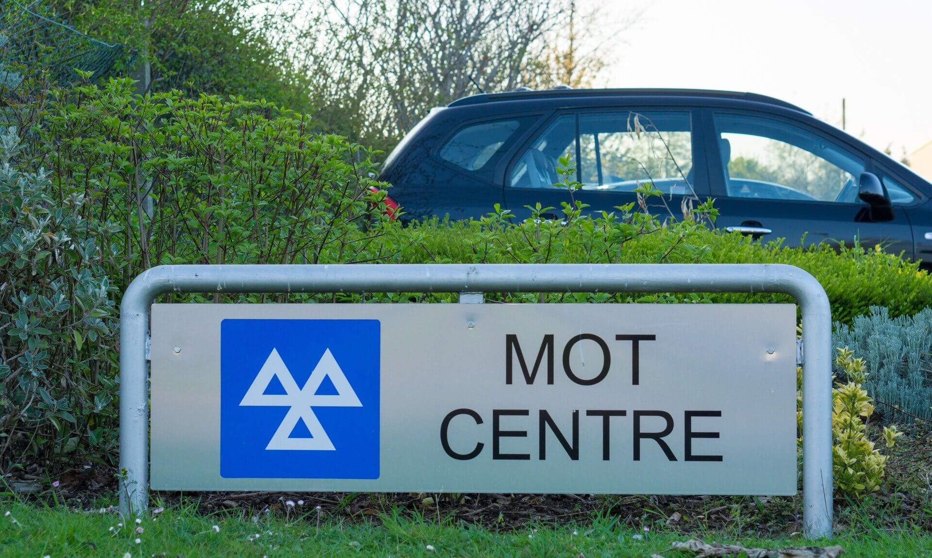 MOT centre sign with a car parked behind a hedge