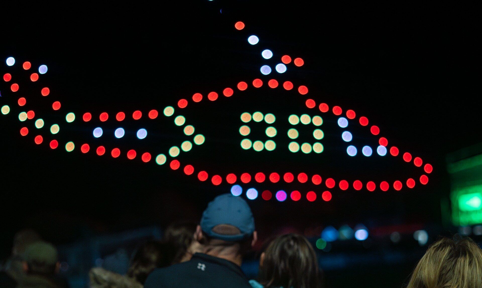 Drones forming a red helicopter shape above a crowd at night