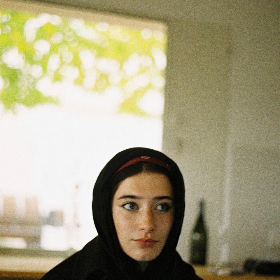 Olive Mills in a black headscarf by a window