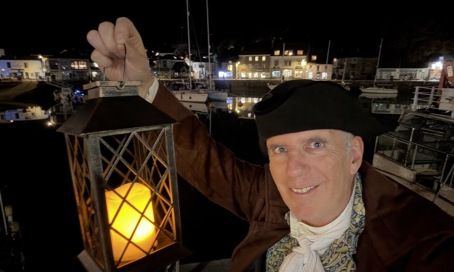 Ghost Walk Padstow guide in 18th-century costume holding a lantern by Padstow Harbour at night