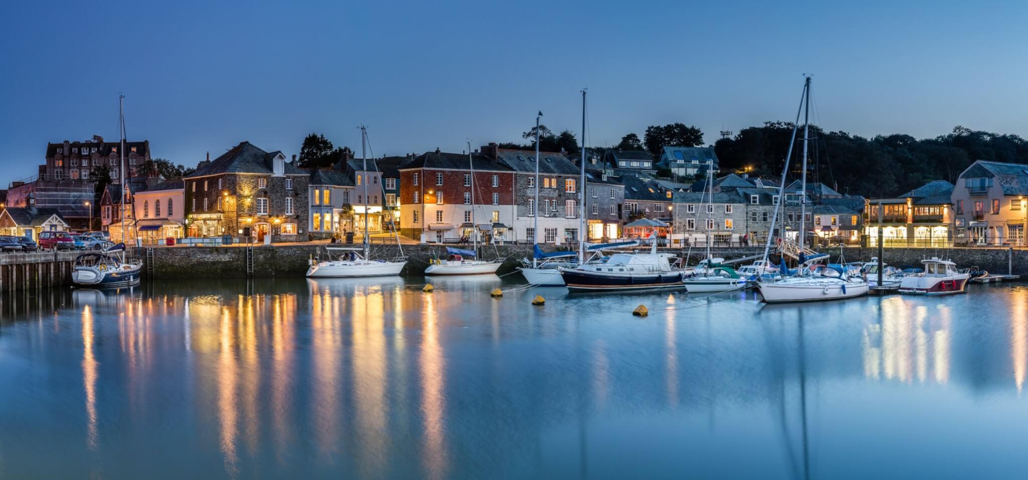 Padstow harbour at dusk with boats moored and lights reflecting on the water