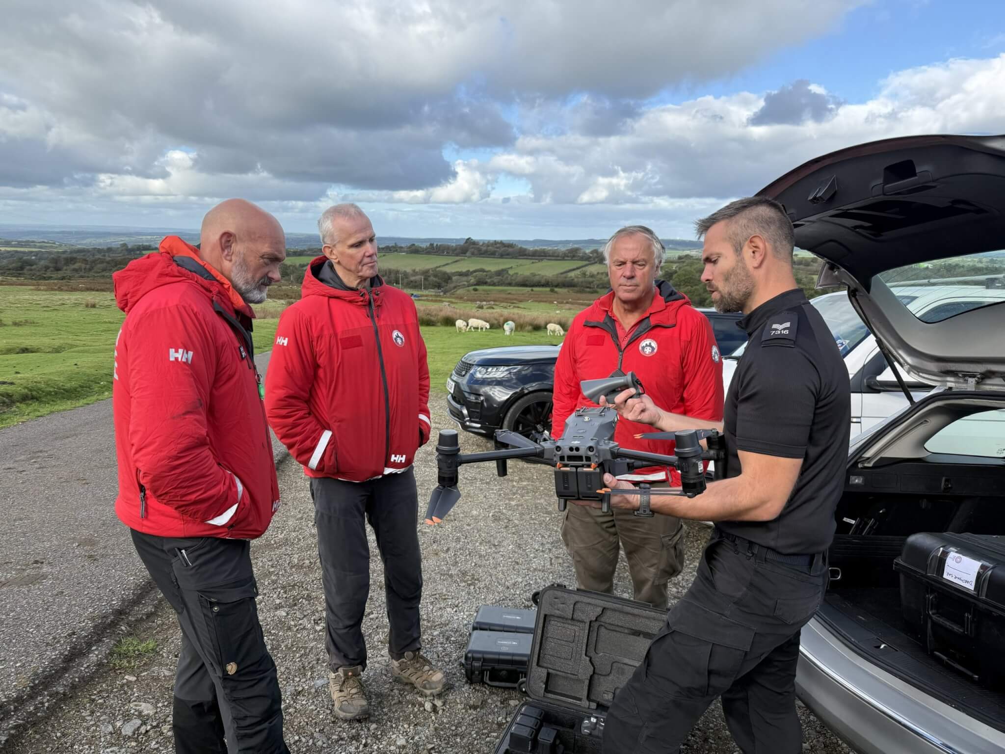 A police officer shows a drone to three search and rescue volunteers in red jackets