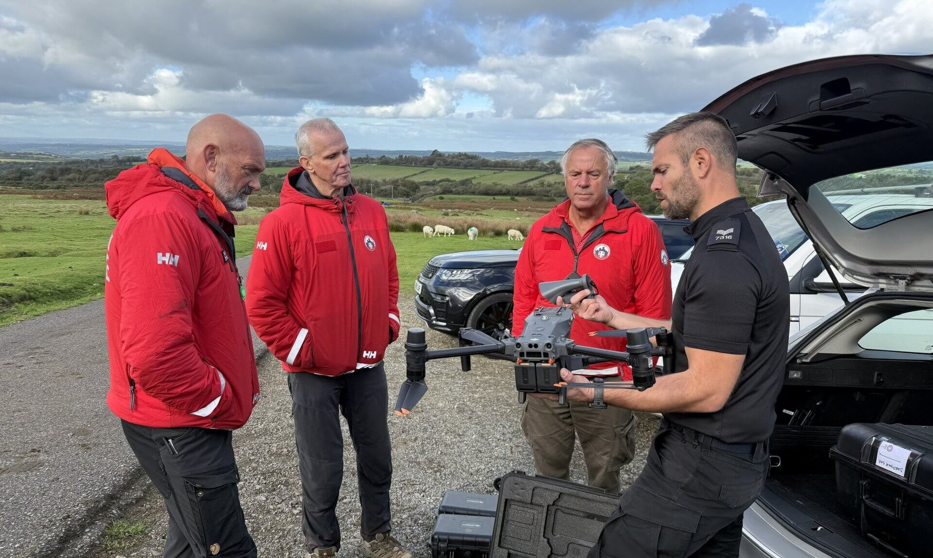 A police officer shows a drone to three search and rescue volunteers in red jackets