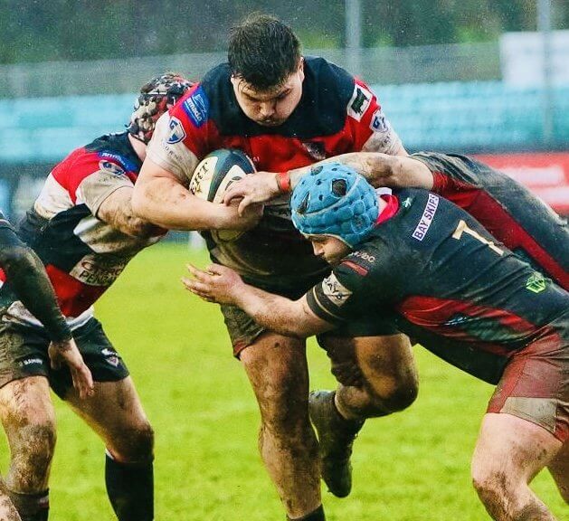 Penzance & Newlyn prop carries the ball into Okehampton defenders on a muddy pitch