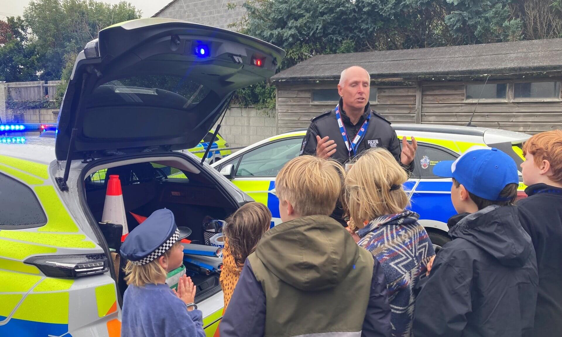 PC Colin Stirling talking to home-schooled children beside a police car at Penzance police station