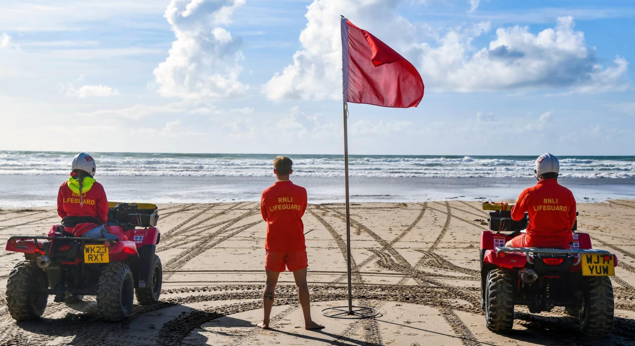 RNLI lifeguards on quad bikes watching the sea beside a red flag at Perran Sands