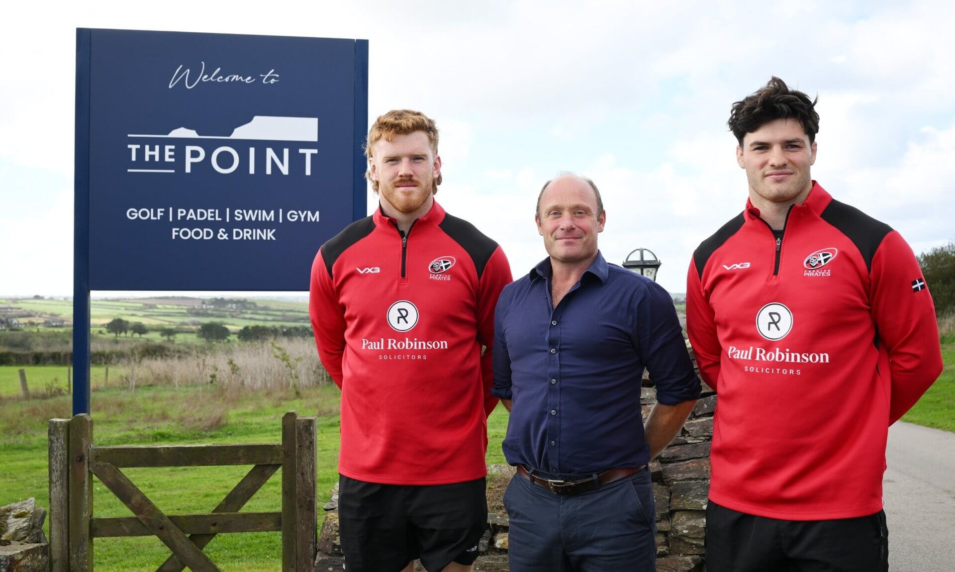 Tom O'Donnell of The Point with two Cornish Pirates players beside the resort's welcome sign at Polzeath