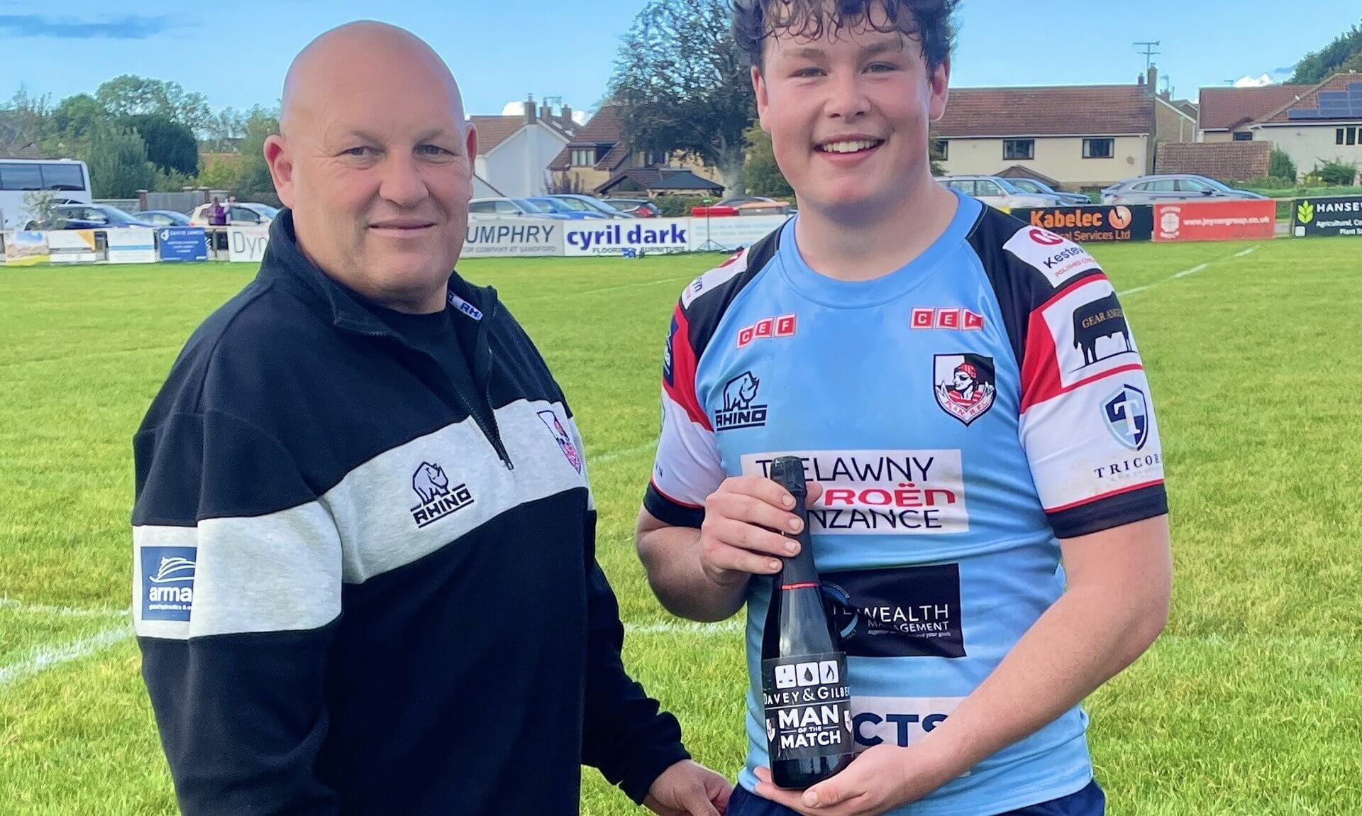 Callum Walsh holding a man of the match bottle beside Andrew Snell on the pitch at Winscombe