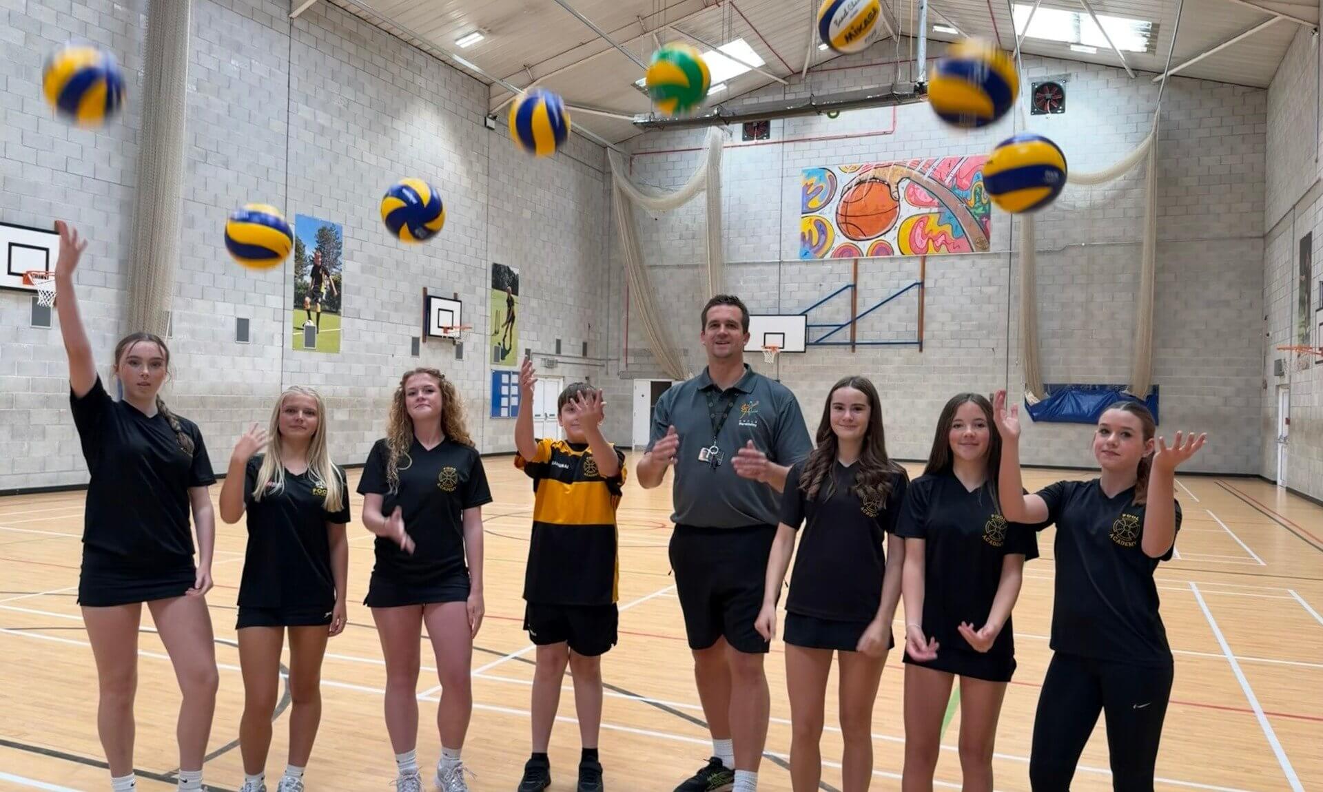 Matt Rogers and Pool Academy students throwing volleyballs in the sports hall