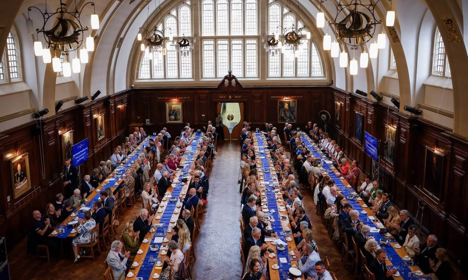 Guests applauding at long tables in the hall at Britannia Royal Naval College, Dartmouth