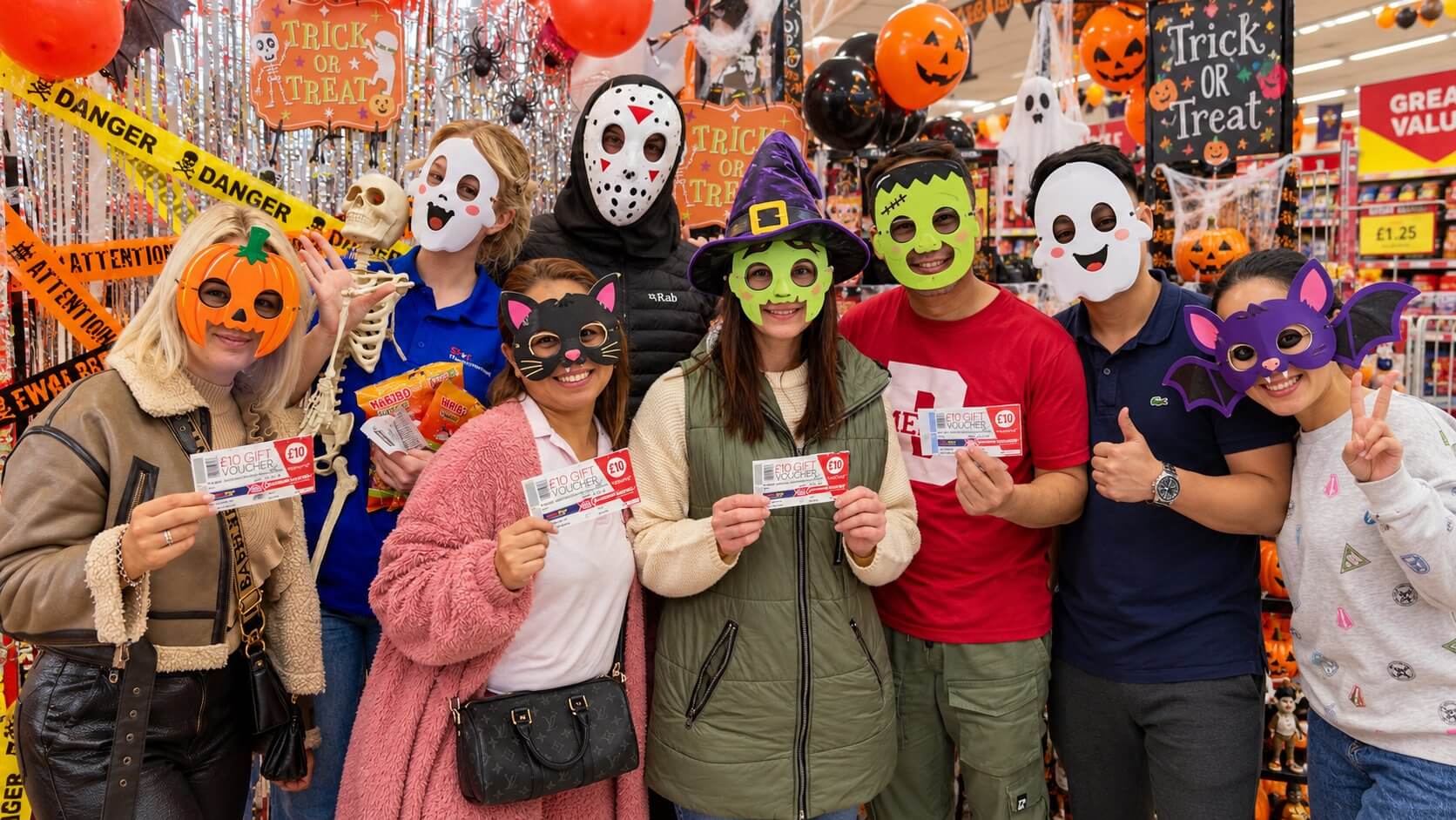 Shoppers and staff in Halloween masks holding £10 Poundstretcher gift vouchers in a store decorated for Halloween