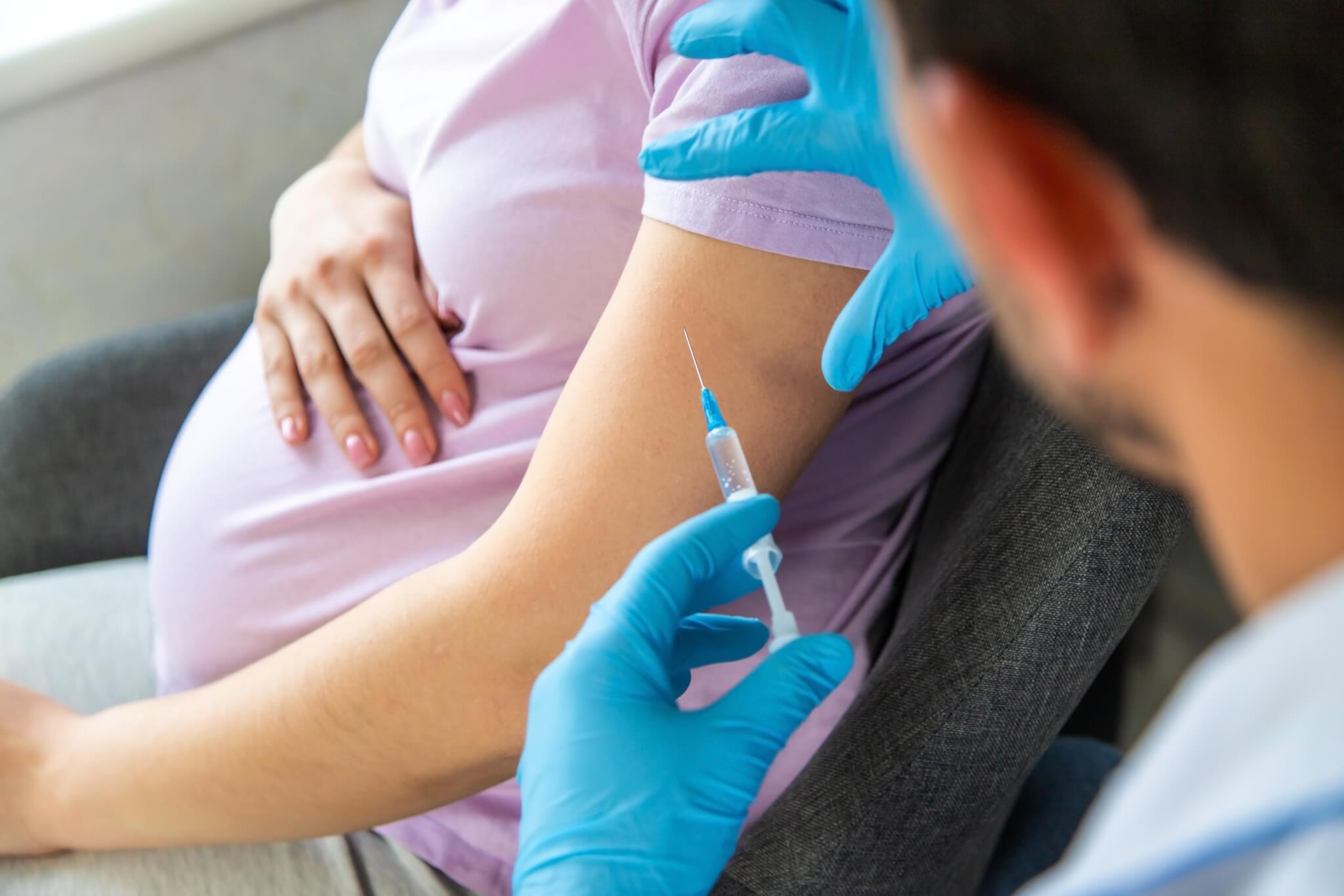 Gloved hands preparing to give a pregnant woman an injection in the arm