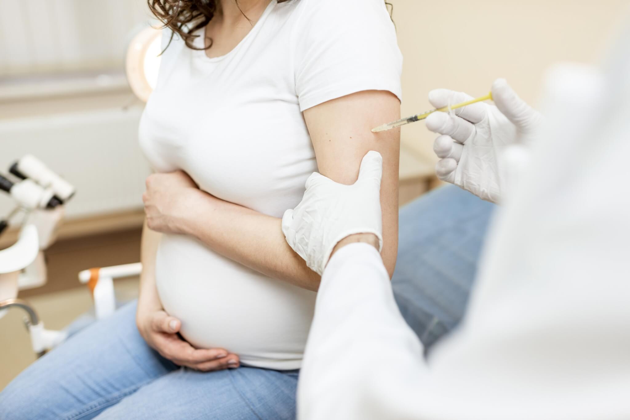 Pregnant woman receiving an injection in her upper arm in a clinic