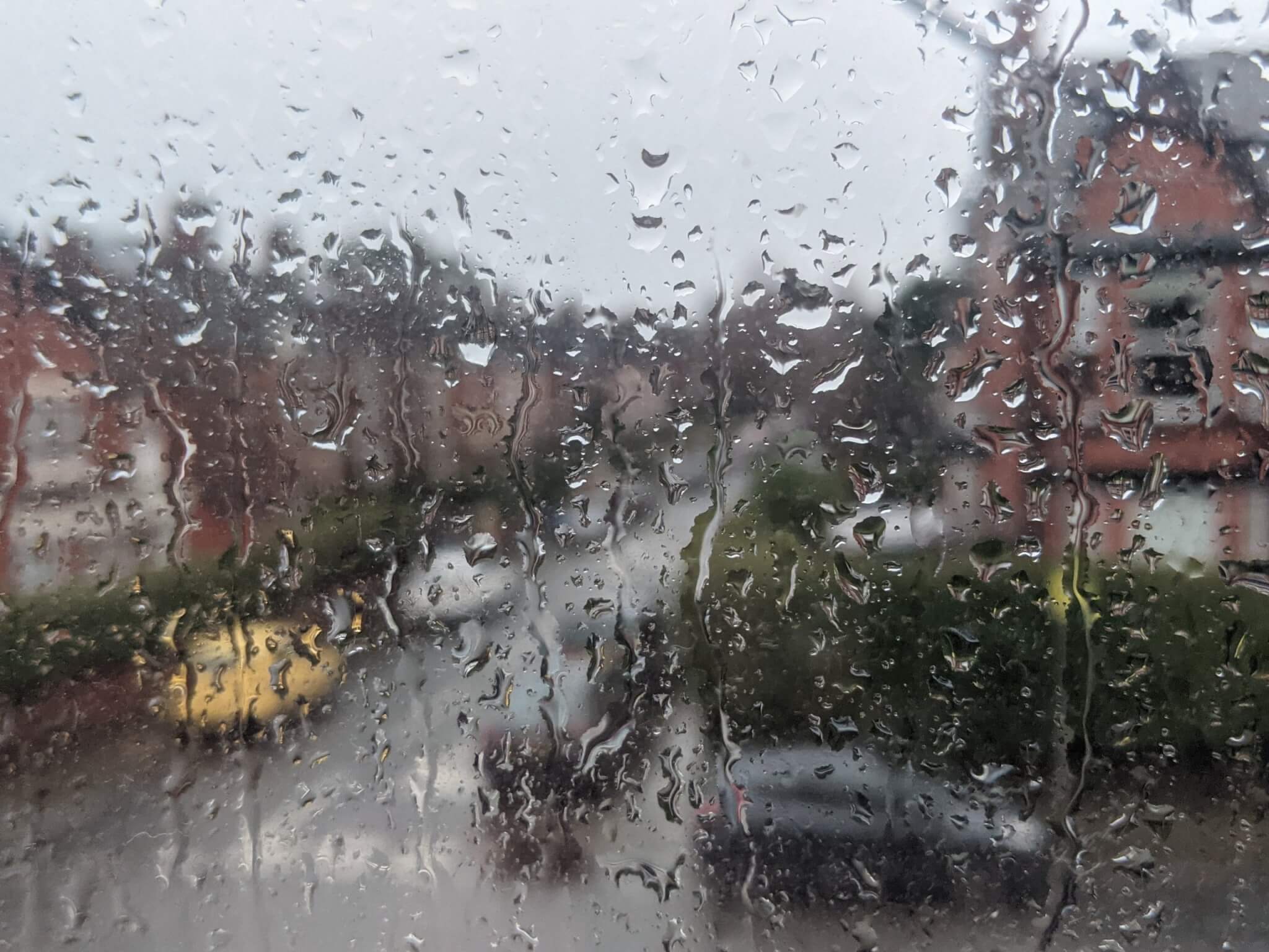 Rain running down a window with houses blurred beyond