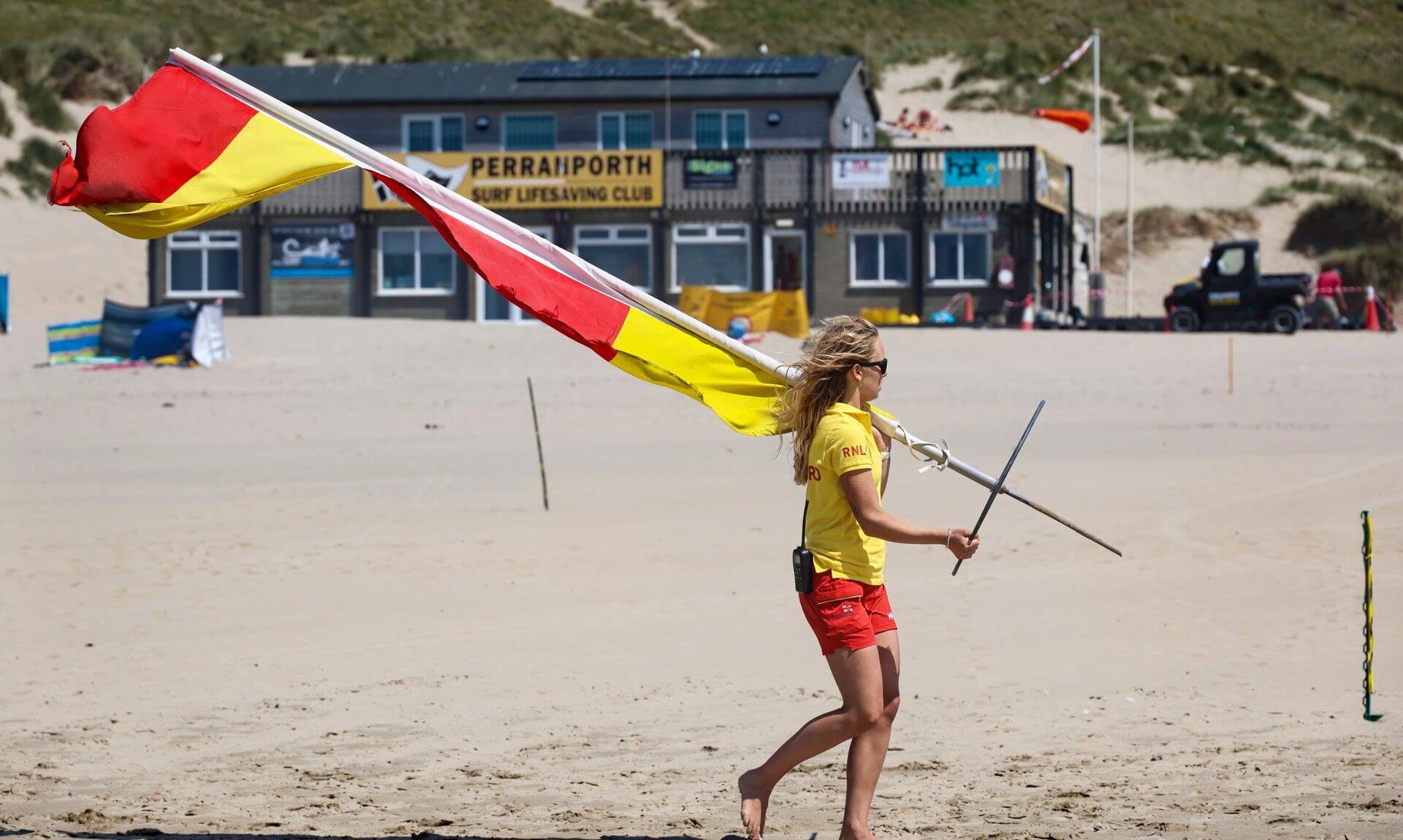 RNLI lifeguard carrying a red and yellow flag on Perranporth beach