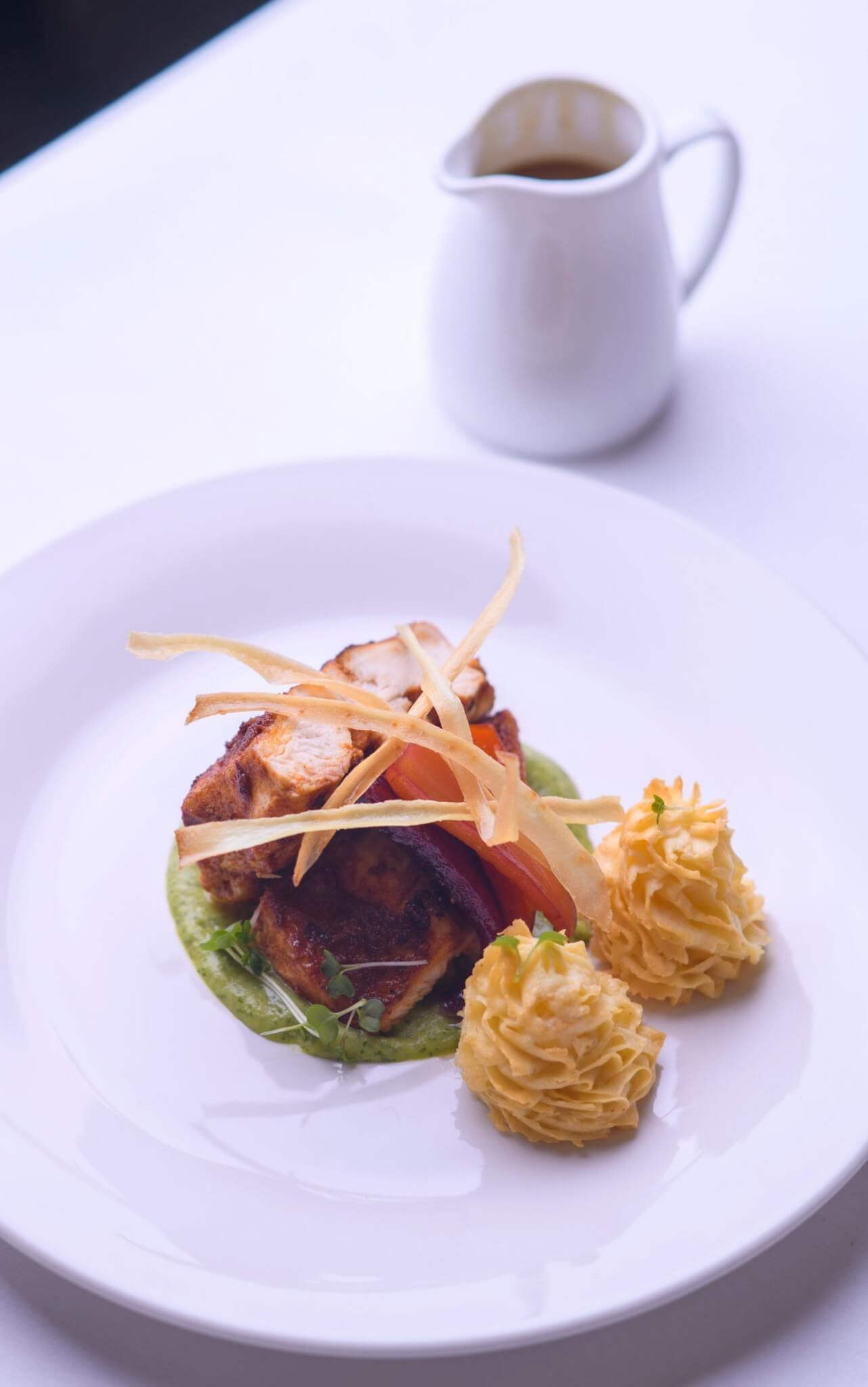 A plated dish of chicken with duchess potatoes and a jug of sauce