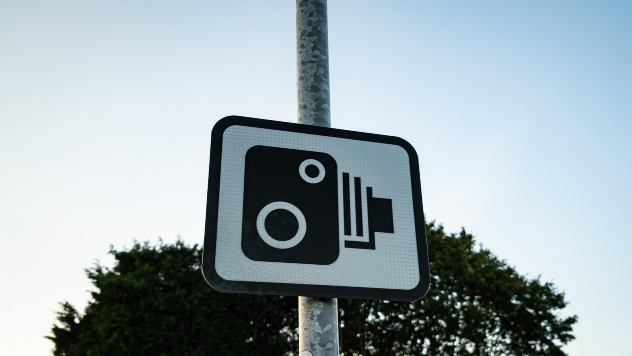 Speed camera warning sign on a pole against a blue sky