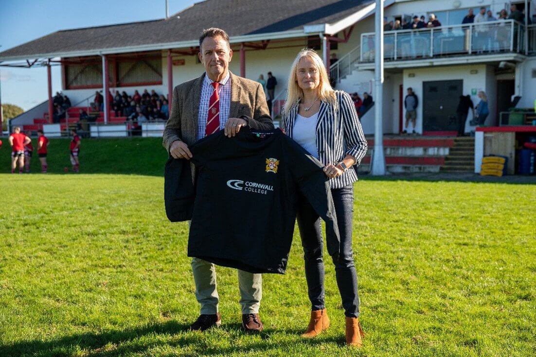 St Austell RFC and Cornwall College representatives holding a club shirt on the pitch