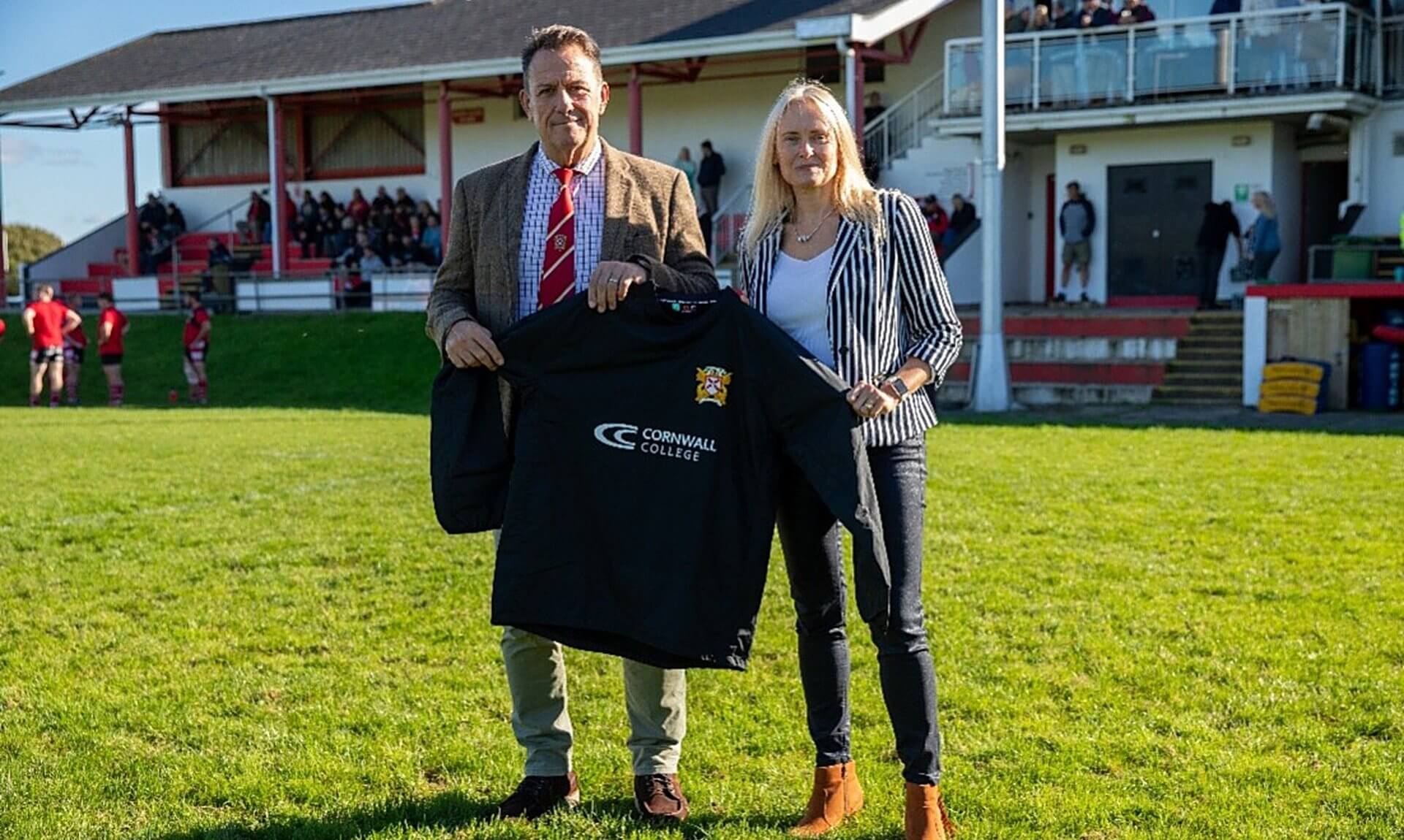 St Austell RFC and Cornwall College representatives holding a club shirt on the pitch