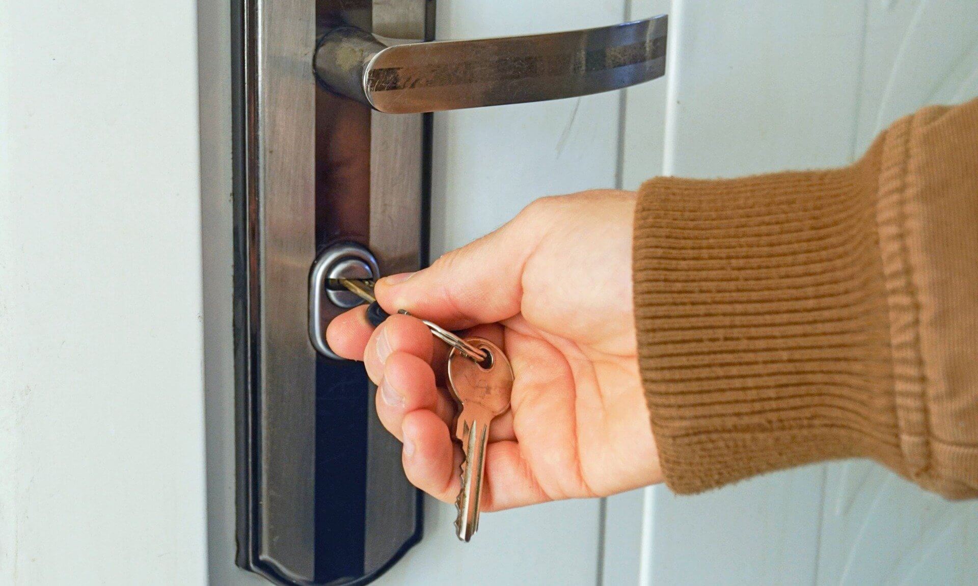 A hand in a brown jumper turning a key in a front door lock