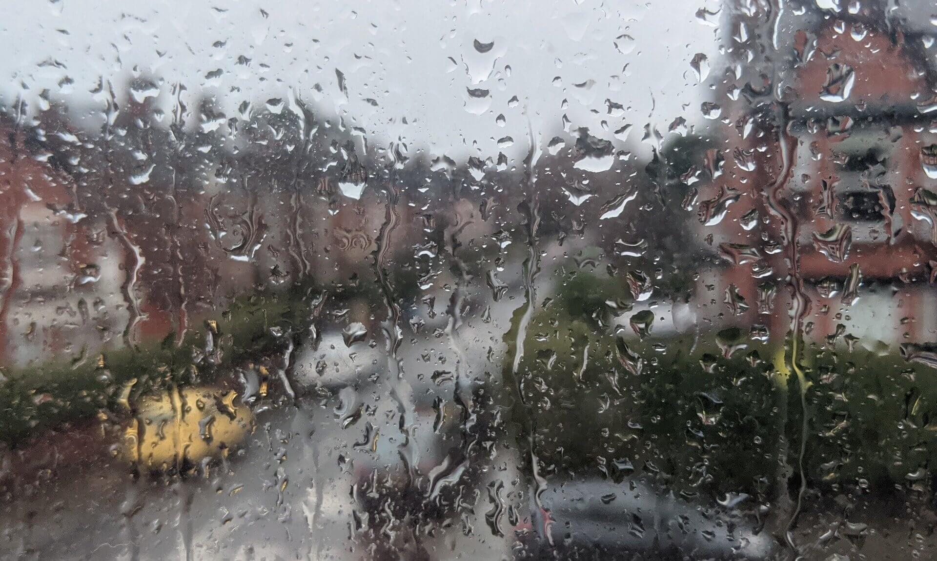 Rain running down a window with houses blurred beyond