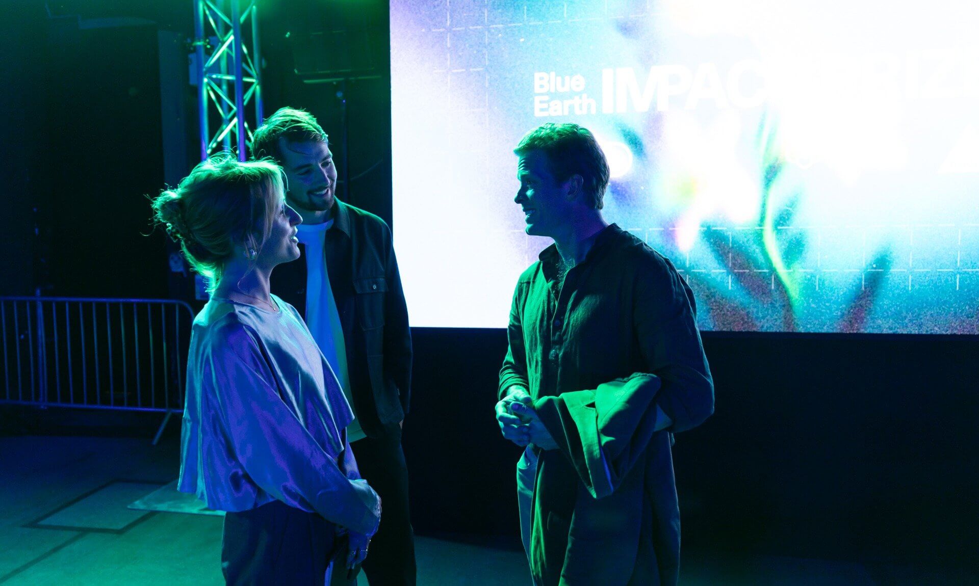 Three people talking in front of the Blue Earth IMPACT Prize screen at Blue Earth Summit