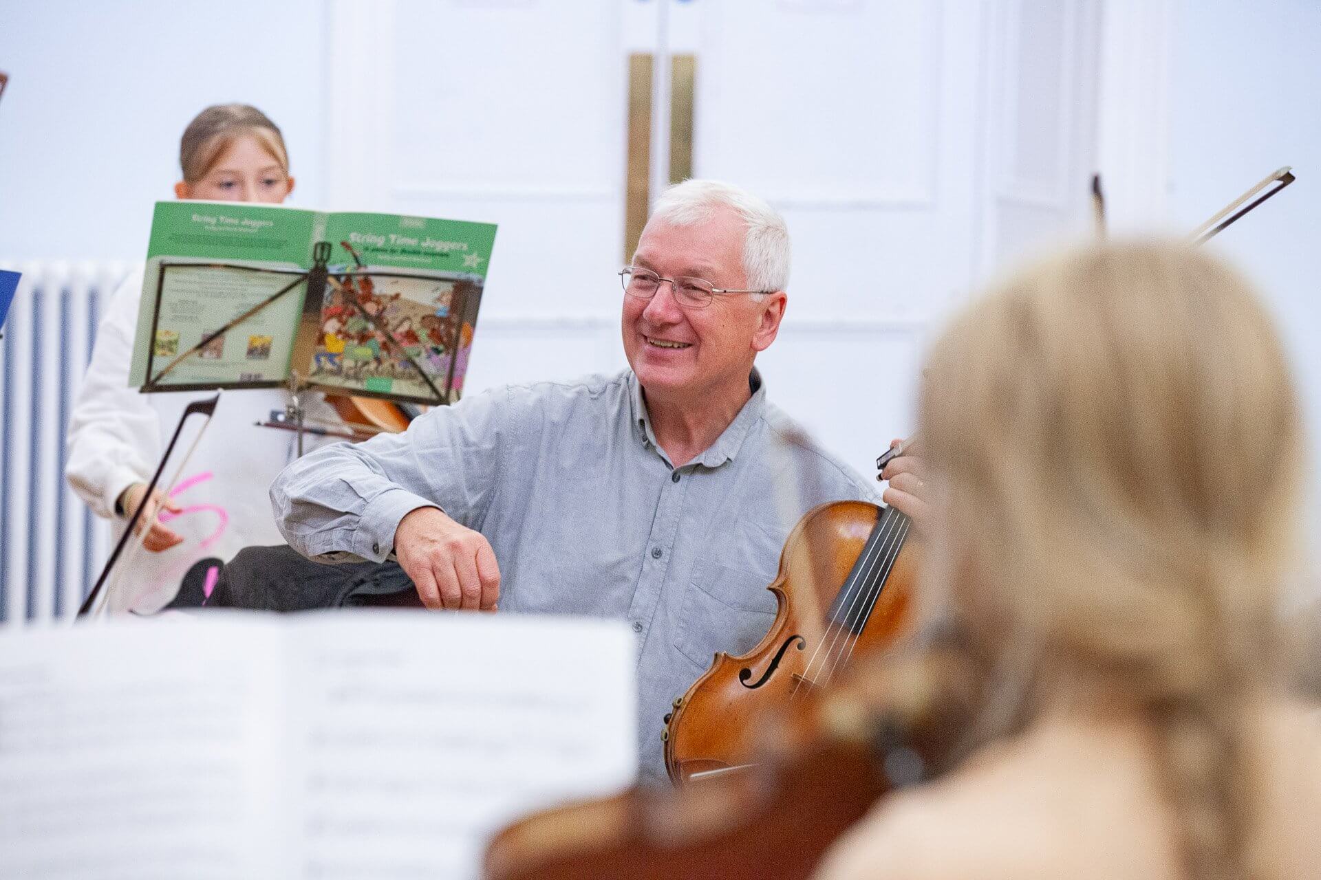 Tim Boulton smiling with a violin during a youth string orchestra rehearsal