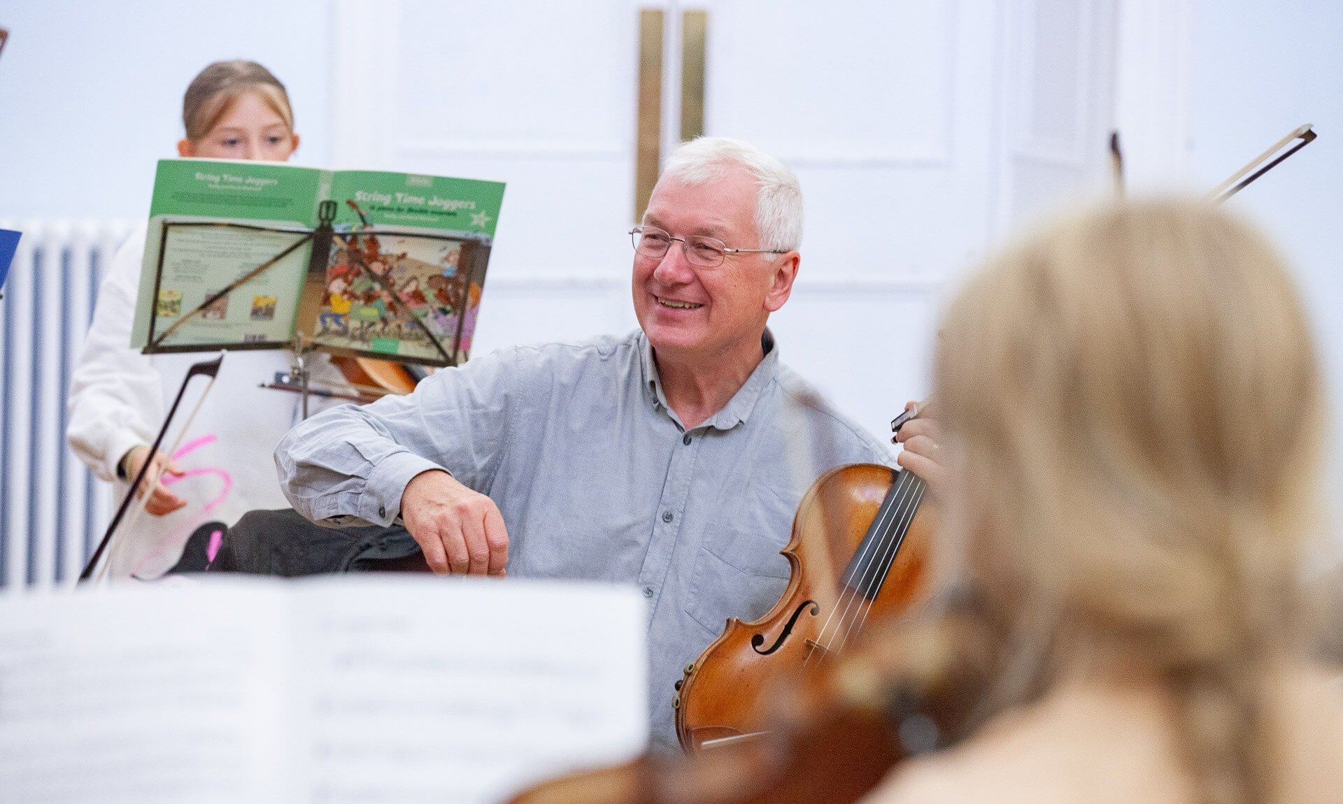 Tim Boulton smiling with a violin during a youth string orchestra rehearsal