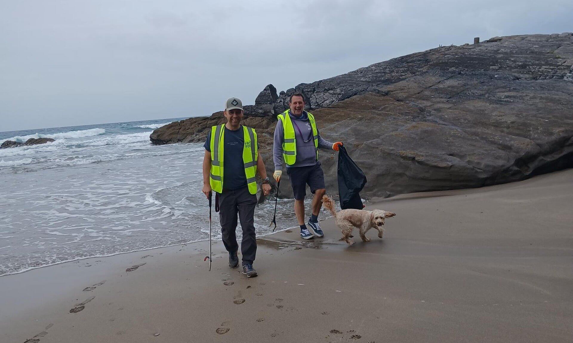 Two beach clean volunteers in hi-vis vests with a dog at Tregonhawke Beach