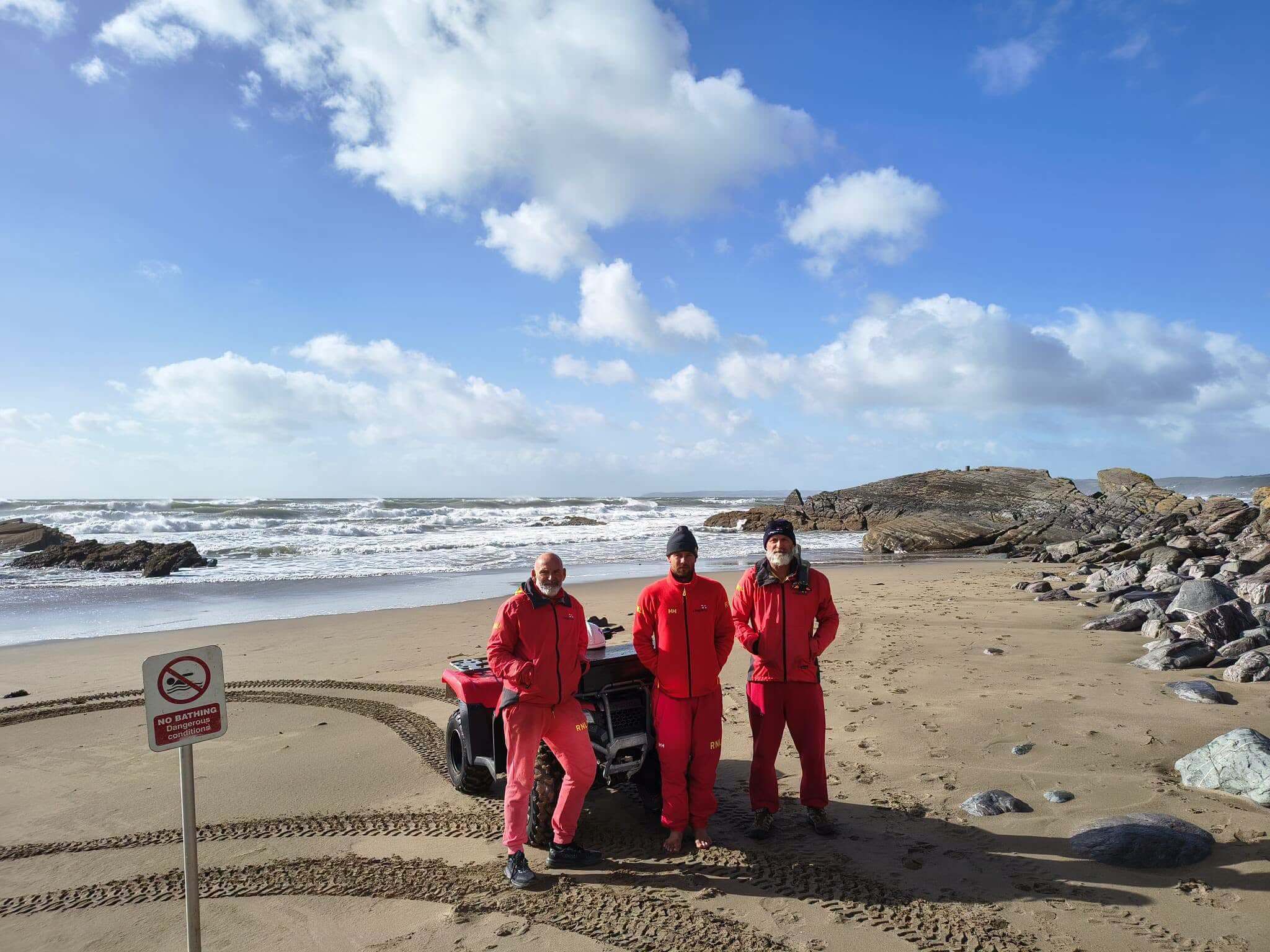Three Tregonhawke RNLI lifeguards on the beach beside a quad bike and a no bathing sign