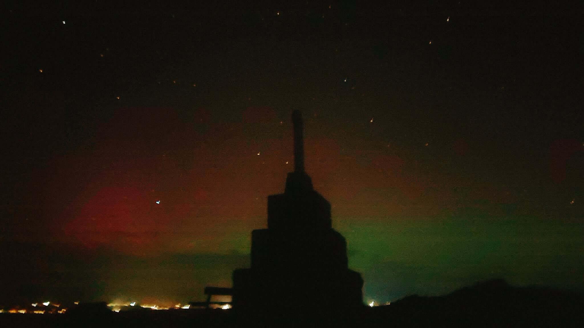 Stone memorial silhouetted against a starry night sky with red and green aurora