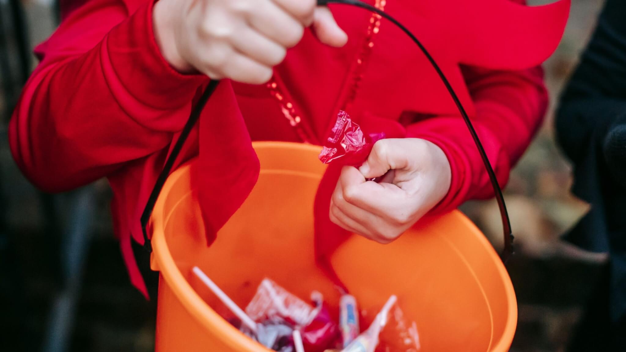Child in a red costume holding an orange bucket of sweets