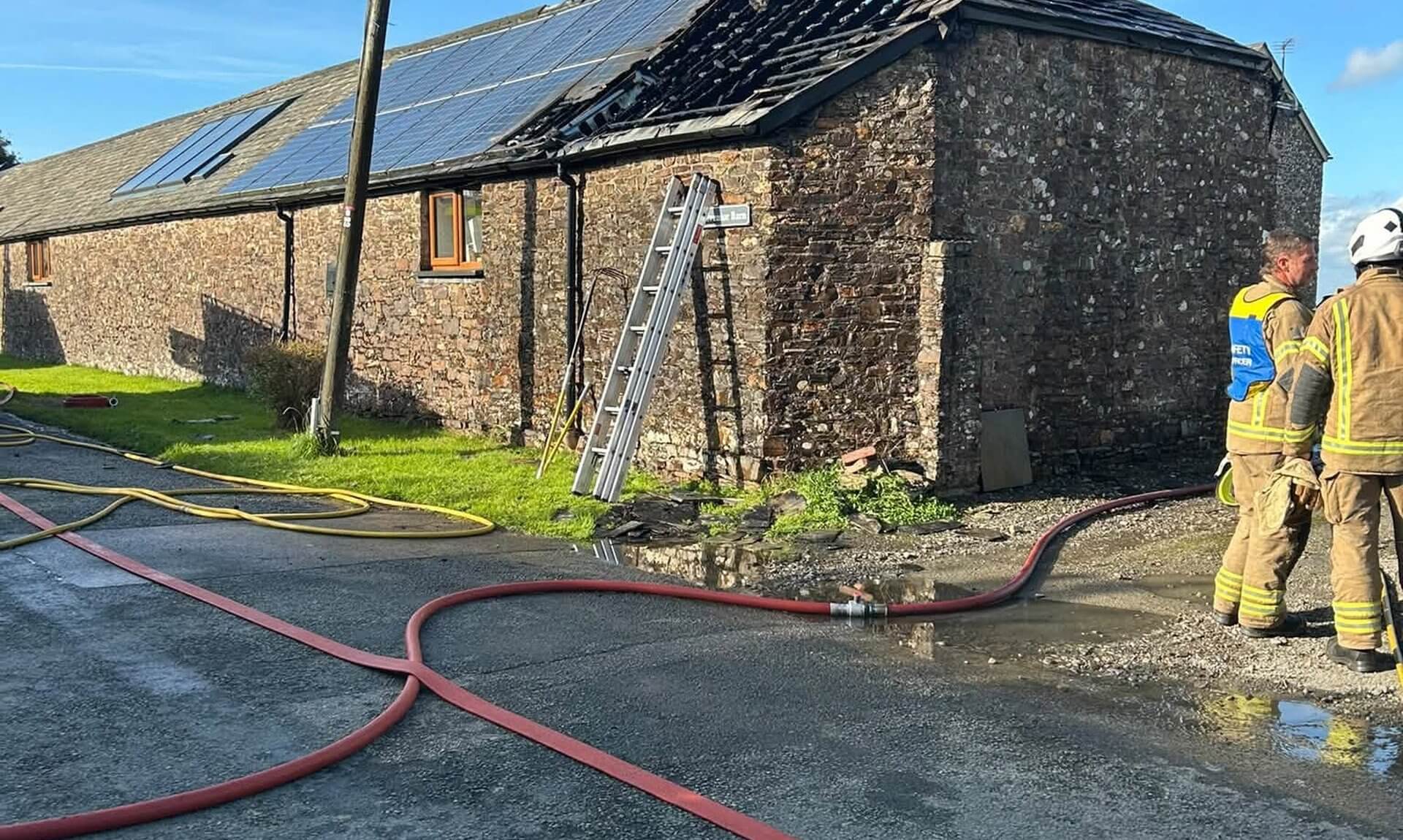 Stone barn conversion near Week St Mary with fire-damaged roof and fire hoses across the road