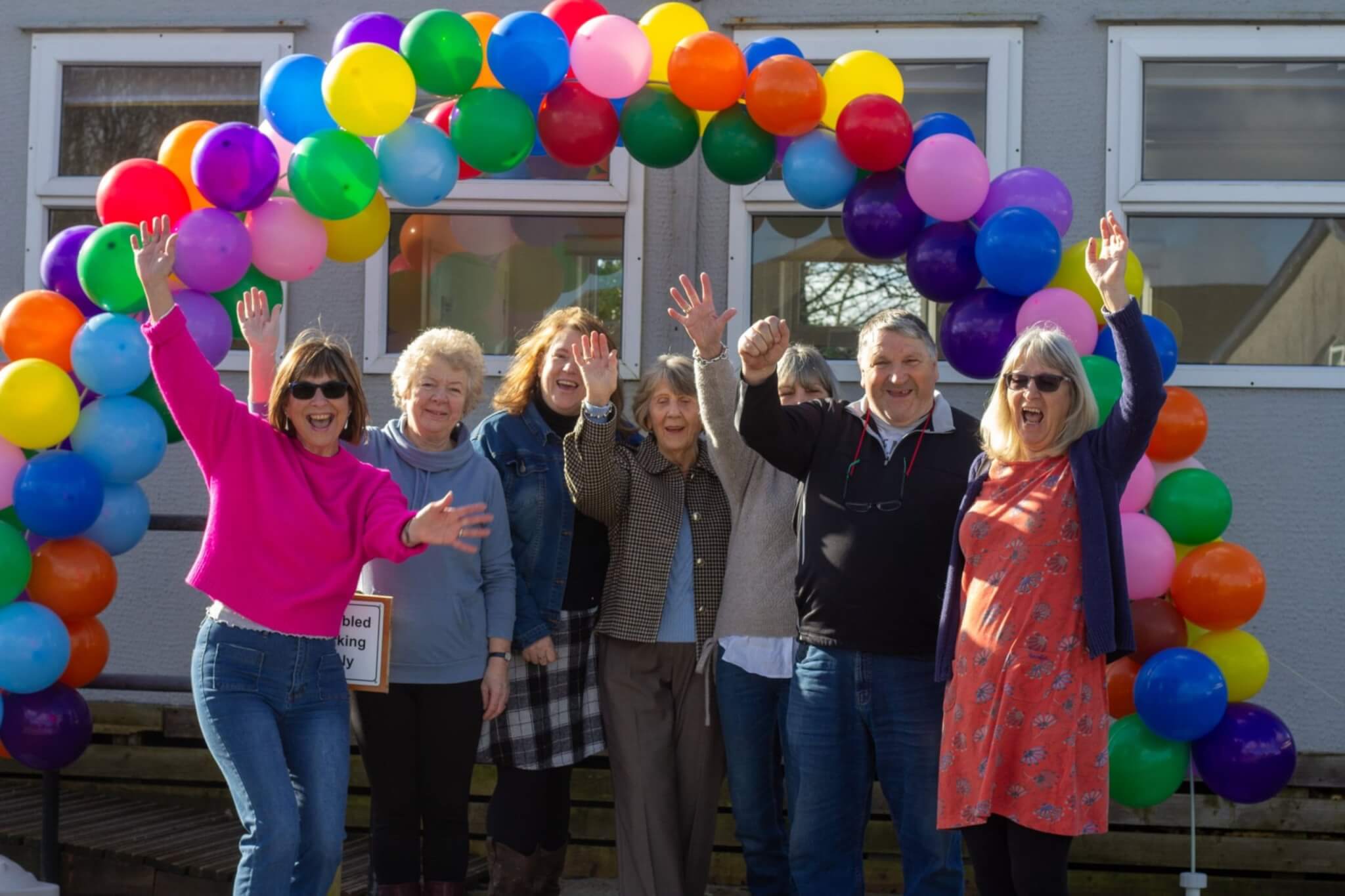 Whitemoor Village Hall committee members cheering under a rainbow balloon arch