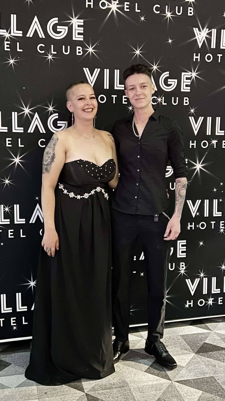Two people in black evening wear in front of a hotel backdrop